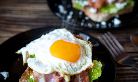 Sandwich with bacon, egg and lettuce on a black plate.