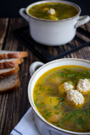 Chicken soup with meatballs and dill in a bowl on a wooden tableの写真素材