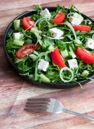 Fresh salad with arugula, tomatoes and feta cheese on wooden backgroundの写真素材