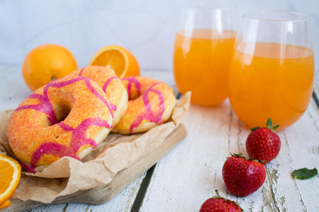 Donuts with strawberry and orange juice on a white wooden table.の写真素材