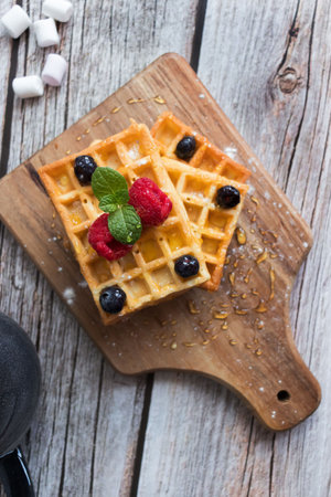 Belgian waffles with fresh berries and sugar on a wooden backgroundの写真素材