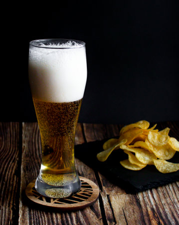 glass of beer with chips on a dark background. tinting. selective focus