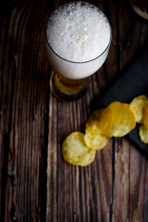 Glass of beer with potato chips on a wooden table. top viewの写真素材