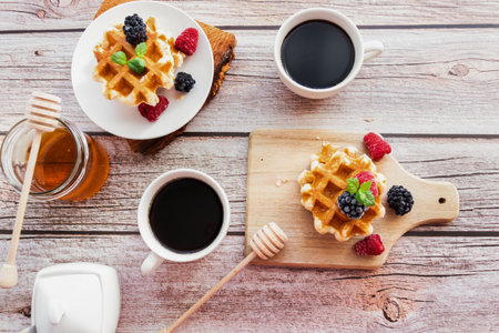 Belgian waffles with fresh berries, honey and coffee on wooden backgroundの写真素材