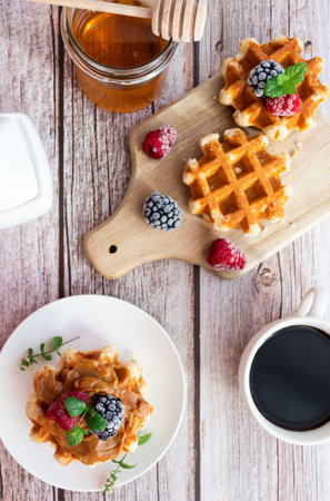Belgian waffles with fresh berries and honey on white wooden backgroundの写真素材