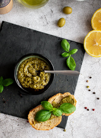Italian pesto sauce with basil leaves, olive oil and lemon slices on a stone backgroundの写真素材