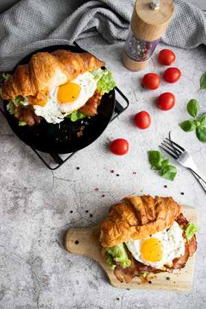 Croissant sandwich with fried egg, bacon, lettuce and tomatoesの写真素材