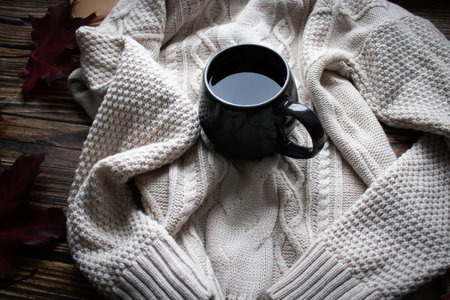 Cup of coffee wrapped in a warm scarf on a wooden background.
