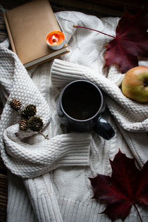 Cup of hot drink, autumn leaves, book and knitted sweater on wooden backgroundの写真素材