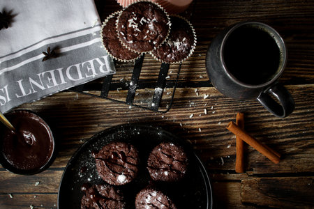 Chocolate muffins with icing sugar and cup of coffee on wooden backgroundの写真素材