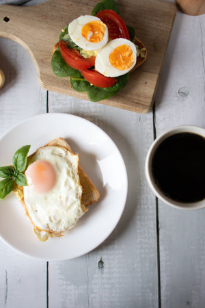 Breakfast with fried eggs, salad and coffee on white wooden tableの写真素材