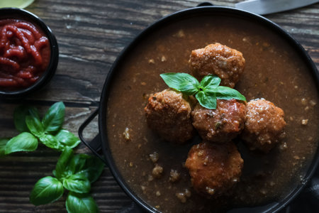 Meatballs with tomato sauce and basil in a black bowl on a wooden tableの写真素材
