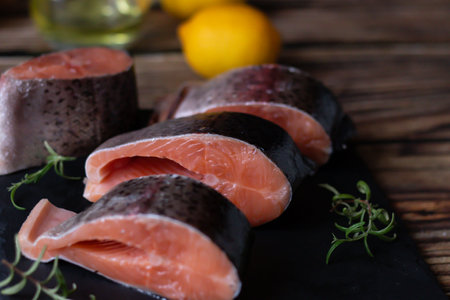 Raw salmon fillets with lemon and herbs on a dark wooden backgroundの写真素材
