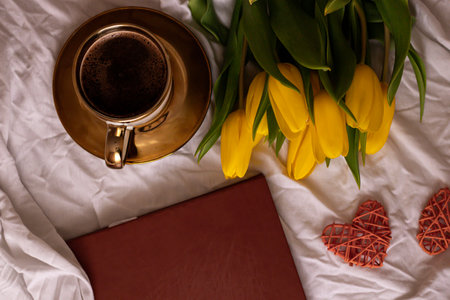 Cup of coffee, book and yellow tulips on the bedの写真素材