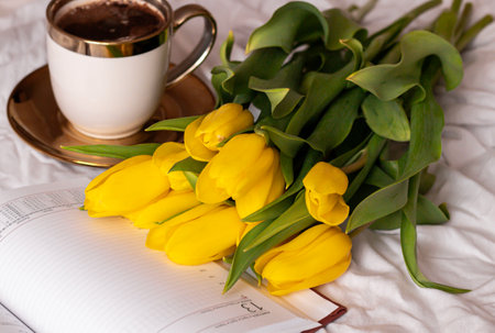 Yellow tulips and a cup of coffee on a white sheet of paperの写真素材