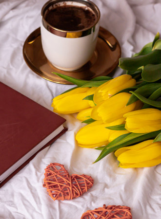 Bouquet of yellow tulips, a cup of hot chocolate and a book on the bed.の写真素材