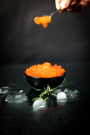 Red caviar in a black bowl with ice on a black background