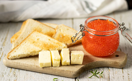 Red caviar in a jar and toast with butter on a wooden boardの写真素材