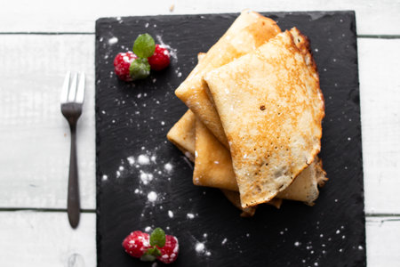 Pancakes with raspberries and mint on a black plate