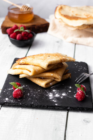 Pancakes with raspberries and honey on a wooden background