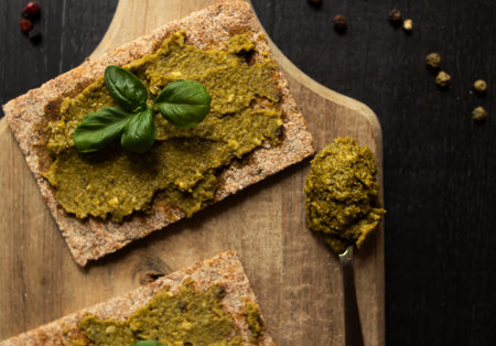 Bread with pesto sauce and basil on a black wooden background