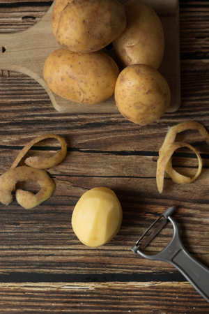 Fresh potatoes on a cutting board and peeler on a wooden backgroundの写真素材