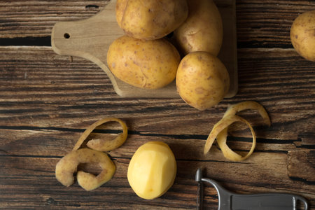 Fresh potatoes and peeler on wooden table, top view. Organic foodの写真素材