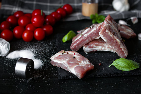 Raw pork ribs with spices and vegetables on a black wooden background.の写真素材