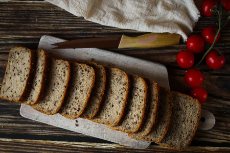 Sliced rye bread on a cutting board with a knife and cherry tomatoes on a wooden background