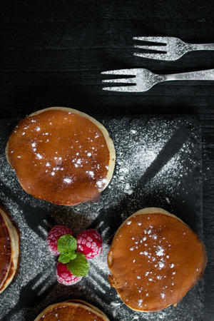 Pancakes with raspberries and powdered sugar on black background