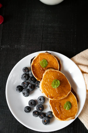 Pancakes with fresh blueberries and maple syrup on a black wooden backgroundの写真素材