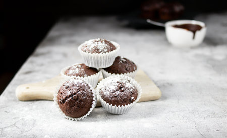 Chocolate muffins with icing sugar on a wooden board, selective focusの写真素材