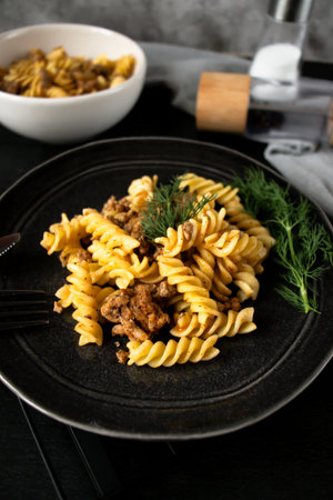 Fusilli pasta with meat and mushrooms on a black plate.の写真素材