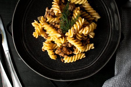 Pasta fusilli with meat and vegetables on black plate.の写真素材