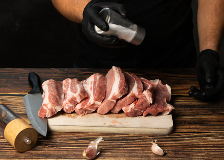 Man's hands in black gloves cut pork meat on a cutting board.の写真素材