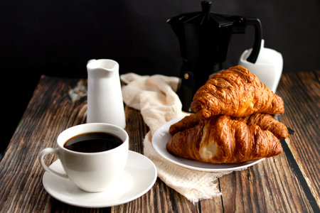 Breakfast with coffee and croissants on a wooden table.の写真素材