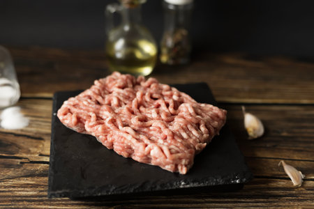 Raw minced meat on black slate board with garlic and oil on wooden table
