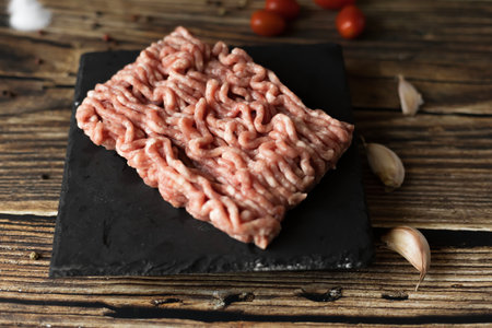 Raw minced meat on a slate plate on a wooden table, top view