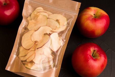 apple chips in a paper bag next to fresh apples on a black background.の写真素材