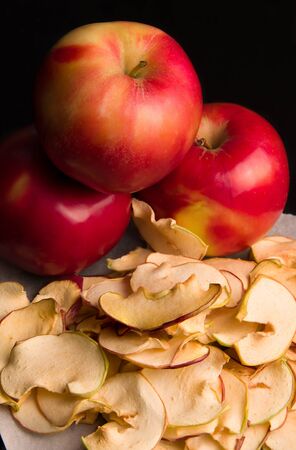 fruit apple chips on a baking paper next to a fresh apple on a black background. natural healthy sweets without sugarの写真素材