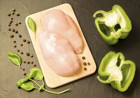 raw chicken fillet on a black background next to basil greens and pepperの写真素材