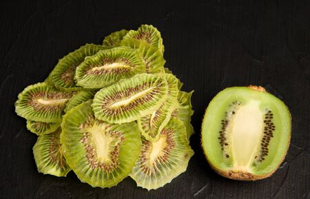 Kiwi fruit chips on a black background next to fresh kimi. healthy sweetsの写真素材