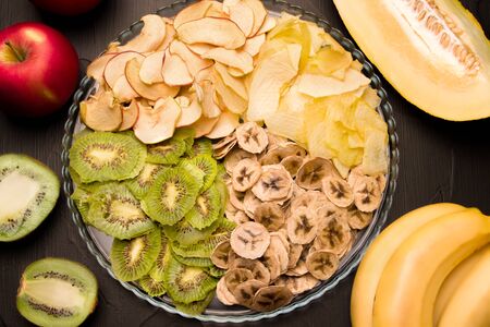 fruit chips on a dish apple, kiwi, banana, pineapple on a black background. Nearby are fresh fruits. Useful snacks. Sweet Sugar Freeの写真素材