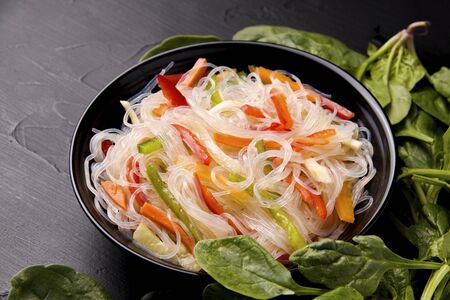 funcho noodles with pepper and carrots in a black plate next to basil on a black backgroundの写真素材