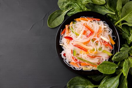 funcho noodles with pepper and carrots in a black plate next to basil on a black background. there is a place for textの写真素材