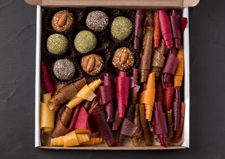 sweet candies energy balls and fruit rolls of dried fruits without sugar in a box on a black backgroundの写真素材