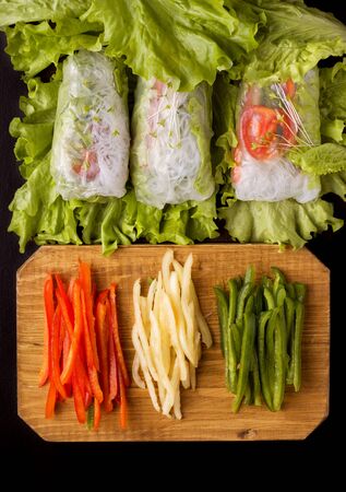 spring rolls with vegetables on a black background. Near the ingredients of chopped pepperの写真素材