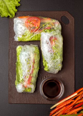 Spring rolls on a wooden board. Near soy sauce, bell peppers and greensの写真素材
