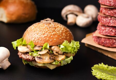 sandwich with meat and mushrooms on a wooden board on a black background next to the ingredientsの写真素材