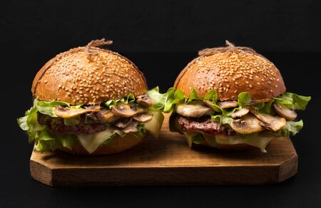 sandwiches with mushrooms and cutlet, cheese and herbs on a wooden board on a black background. fast...
